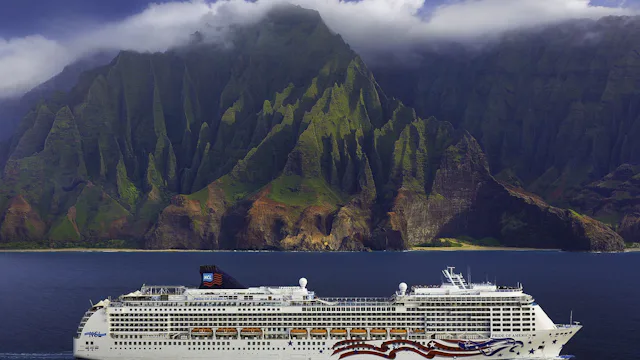 Cruiseskip fra Norwegian Cruise Line ved Hawaii med utsikt mot grønne fjell og kystlinje